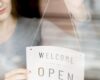 woman-putting-open-sign-window-coffee-shop