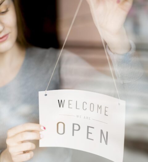 woman-putting-open-sign-window-coffee-shop